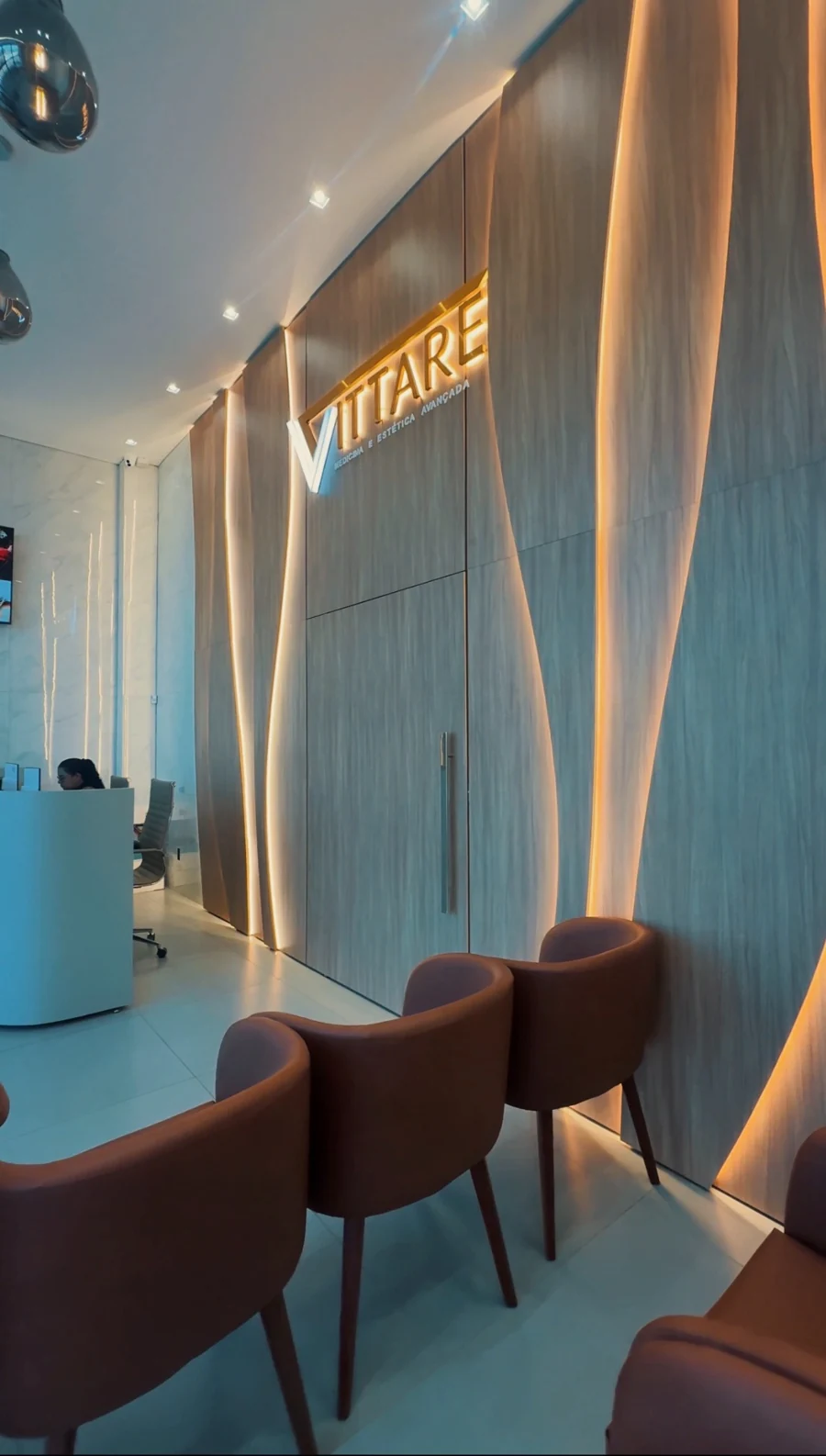 Sala de espera da Vittare com poltronas, painel de madeira e iluminação acolhedora.